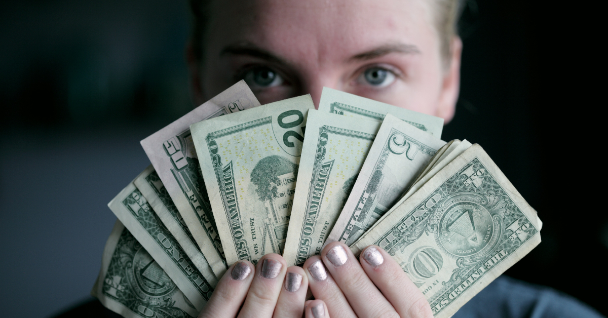 Person holding fan of cash infront of face