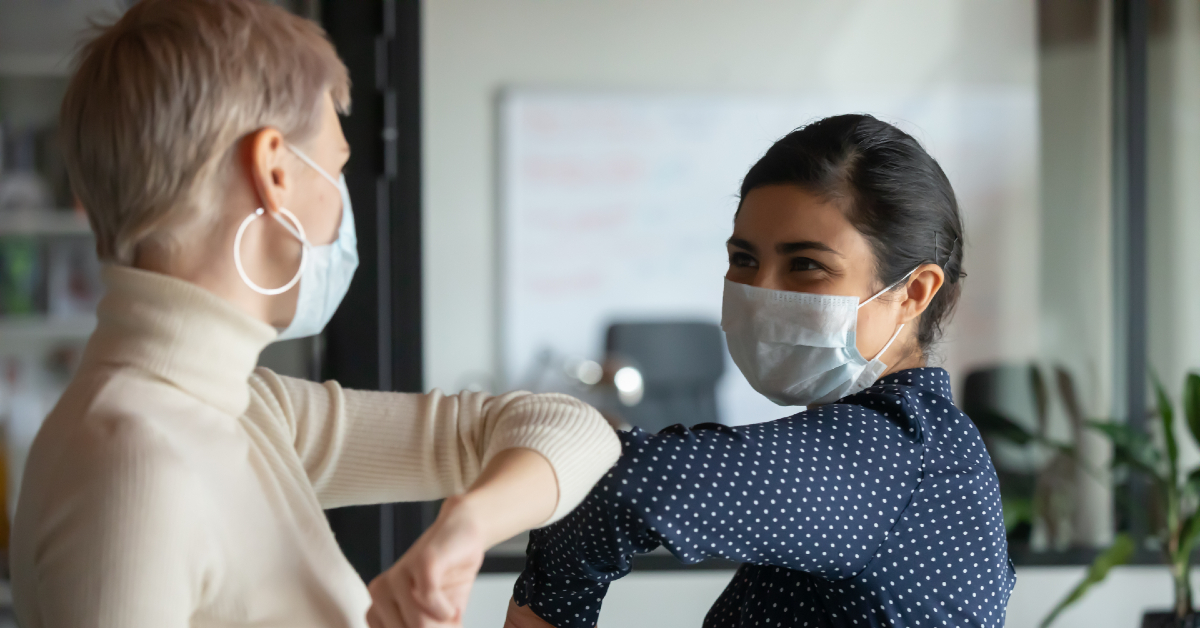 two women in masks touching elbows